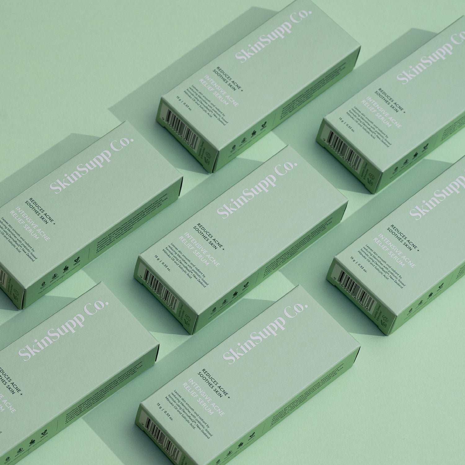 Multiple green unit cartons of SkinSupp Co. Intensive Acne Relief Serum arranged on green table 
